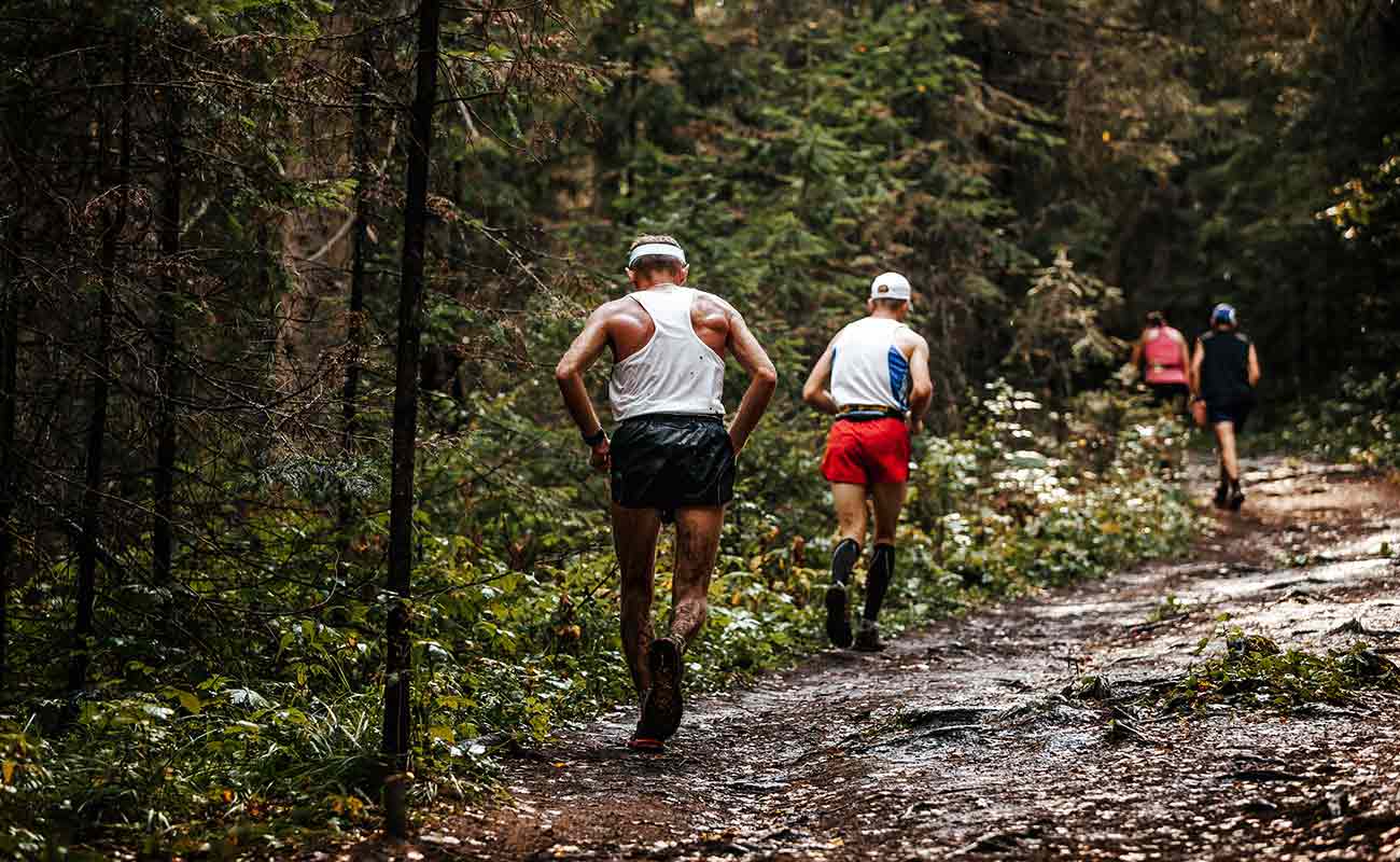 A group of people running on a trail in the woods.