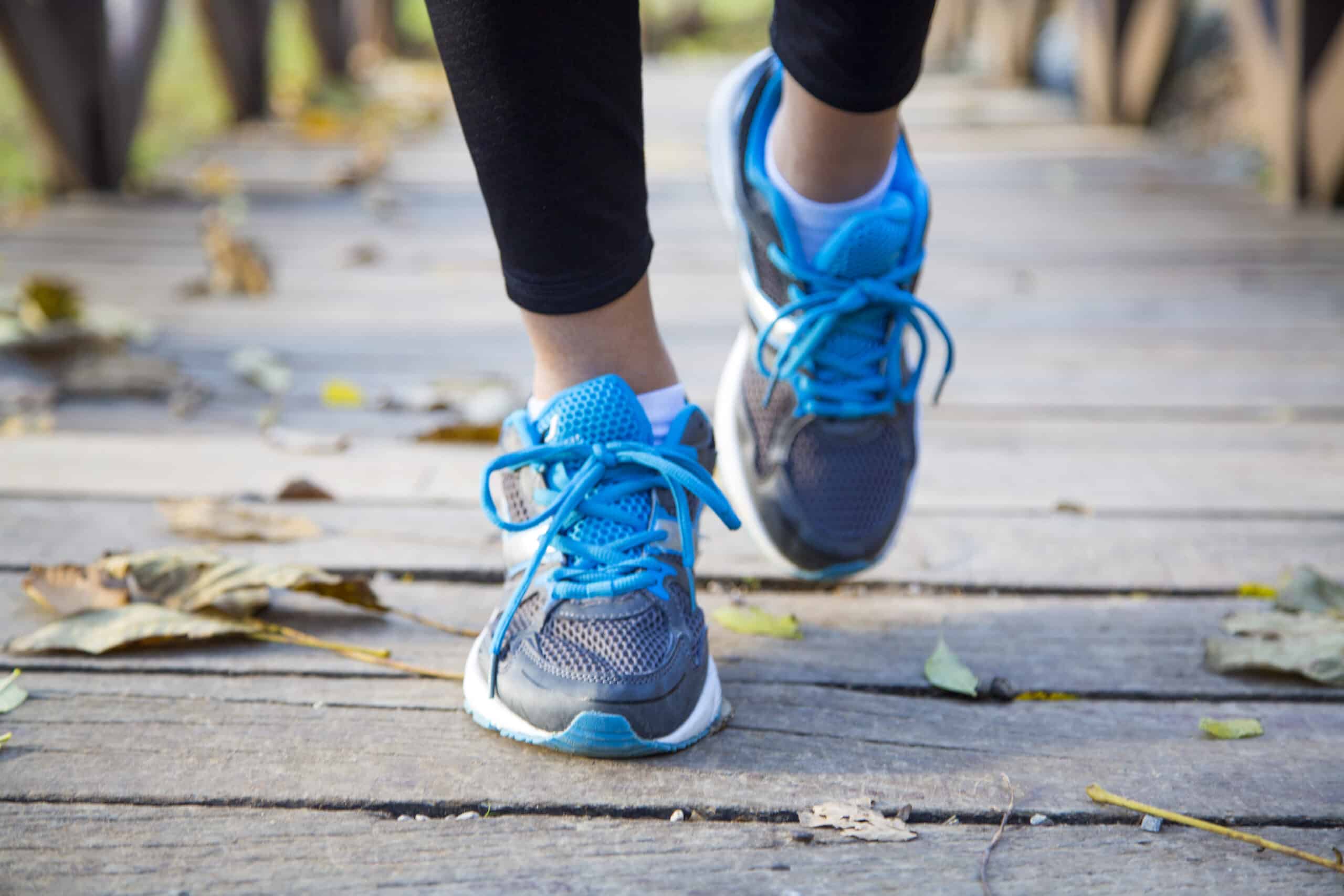 A woman participating in a spring race is walking on a wooden bridge wearing blue running shoes.