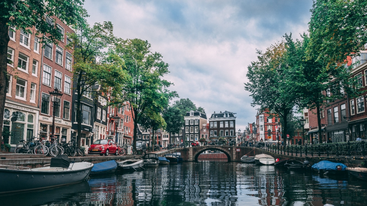 A picturesque canal in Amsterdam with boats and trees in the background.