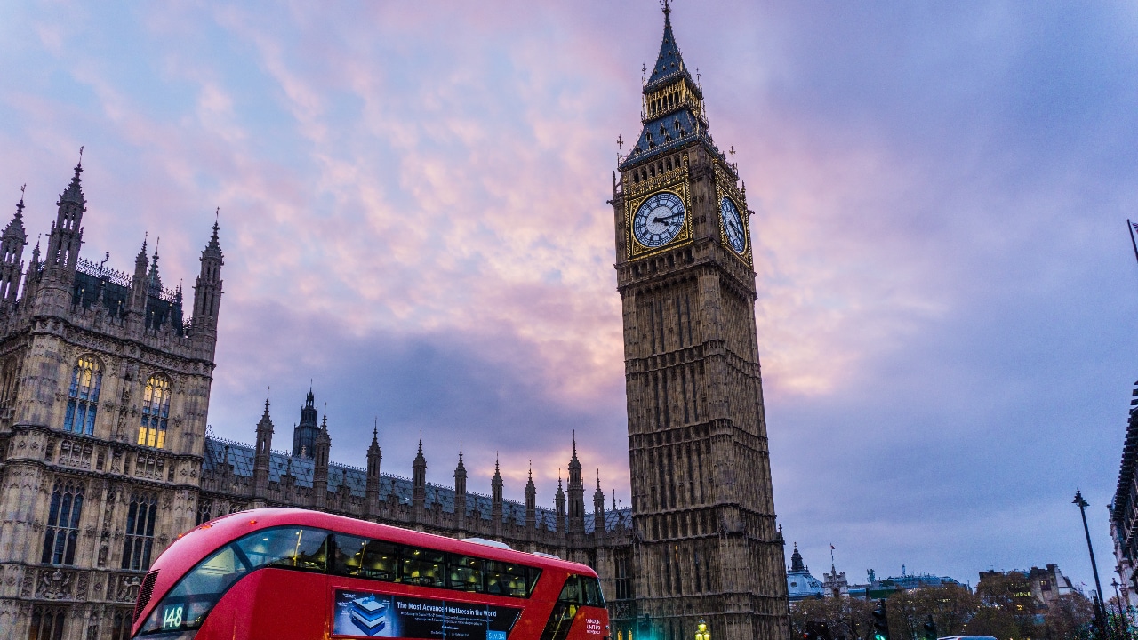 A red double decker bus driving past big ben.