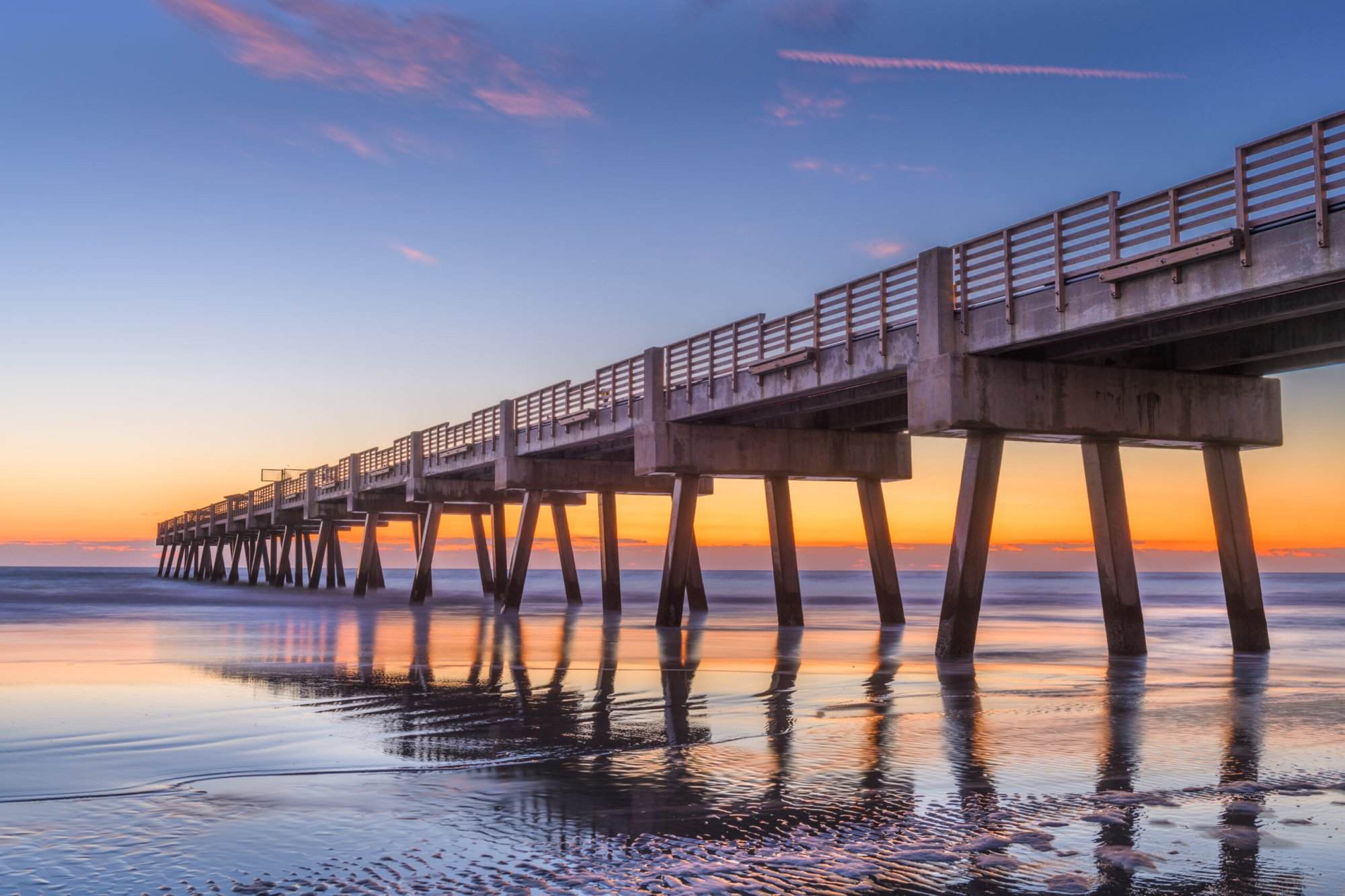 A pier at sunset with water and sand in the background.