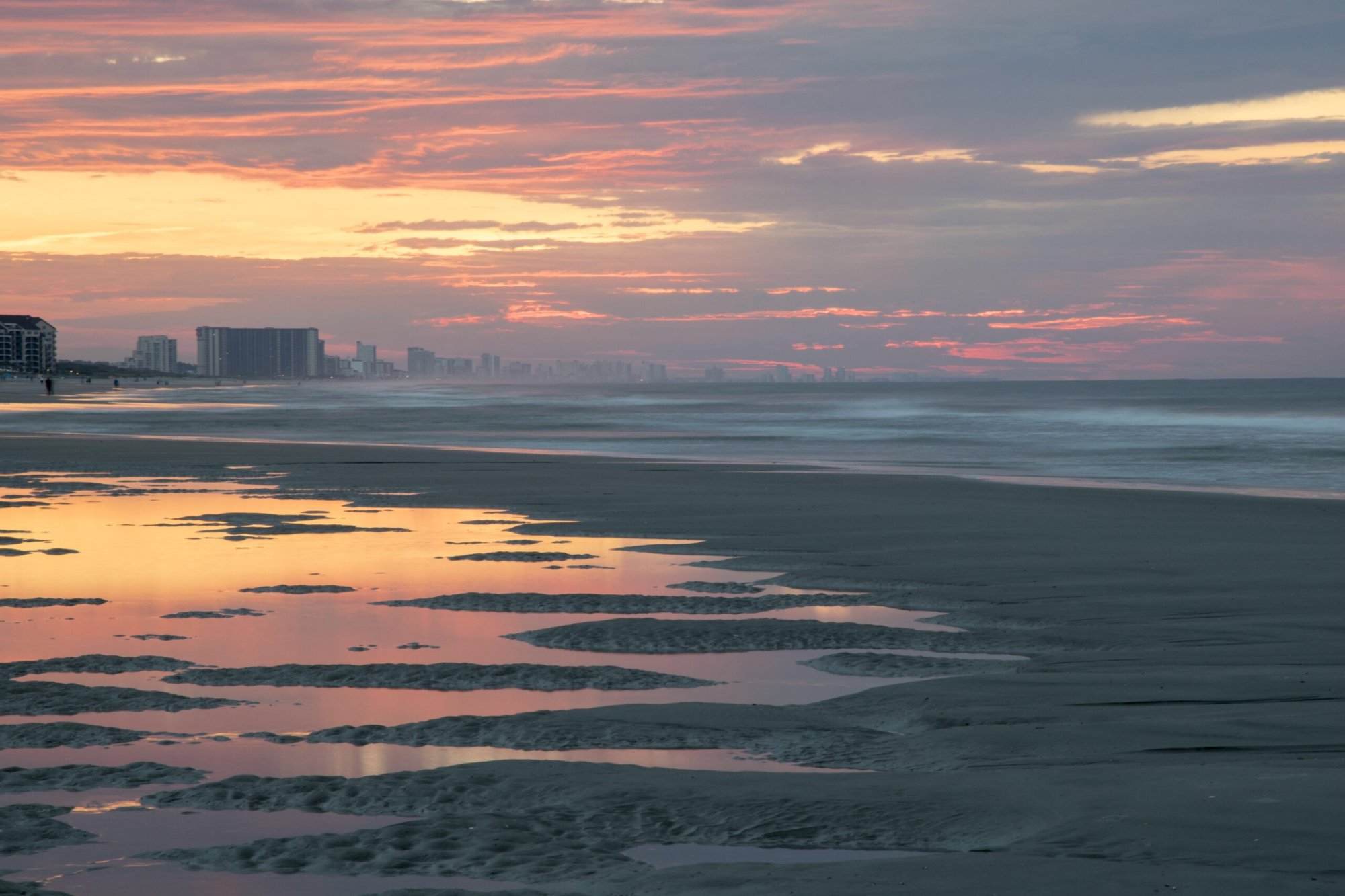 A beach at sunset with buildings in the background.