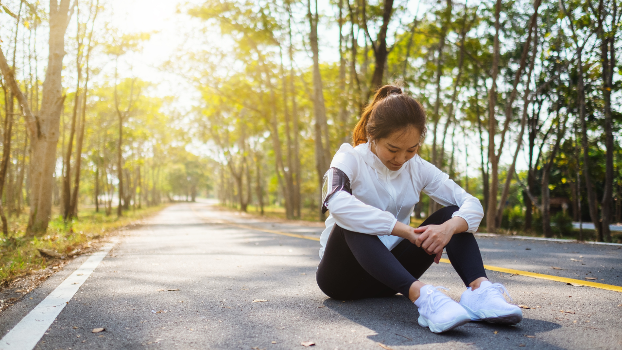 A woman, surrounded by weary runners, sits solemnly on the side of a road, her face expressing post-race sadness.