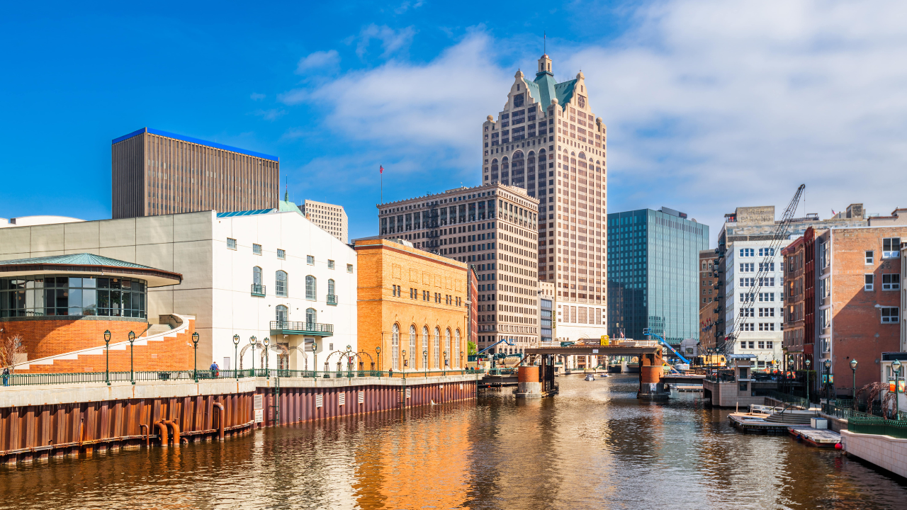 View of a city riverfront featuring modern and historical buildings under a clear blue sky during the Milwaukee Lakefront Marathon.