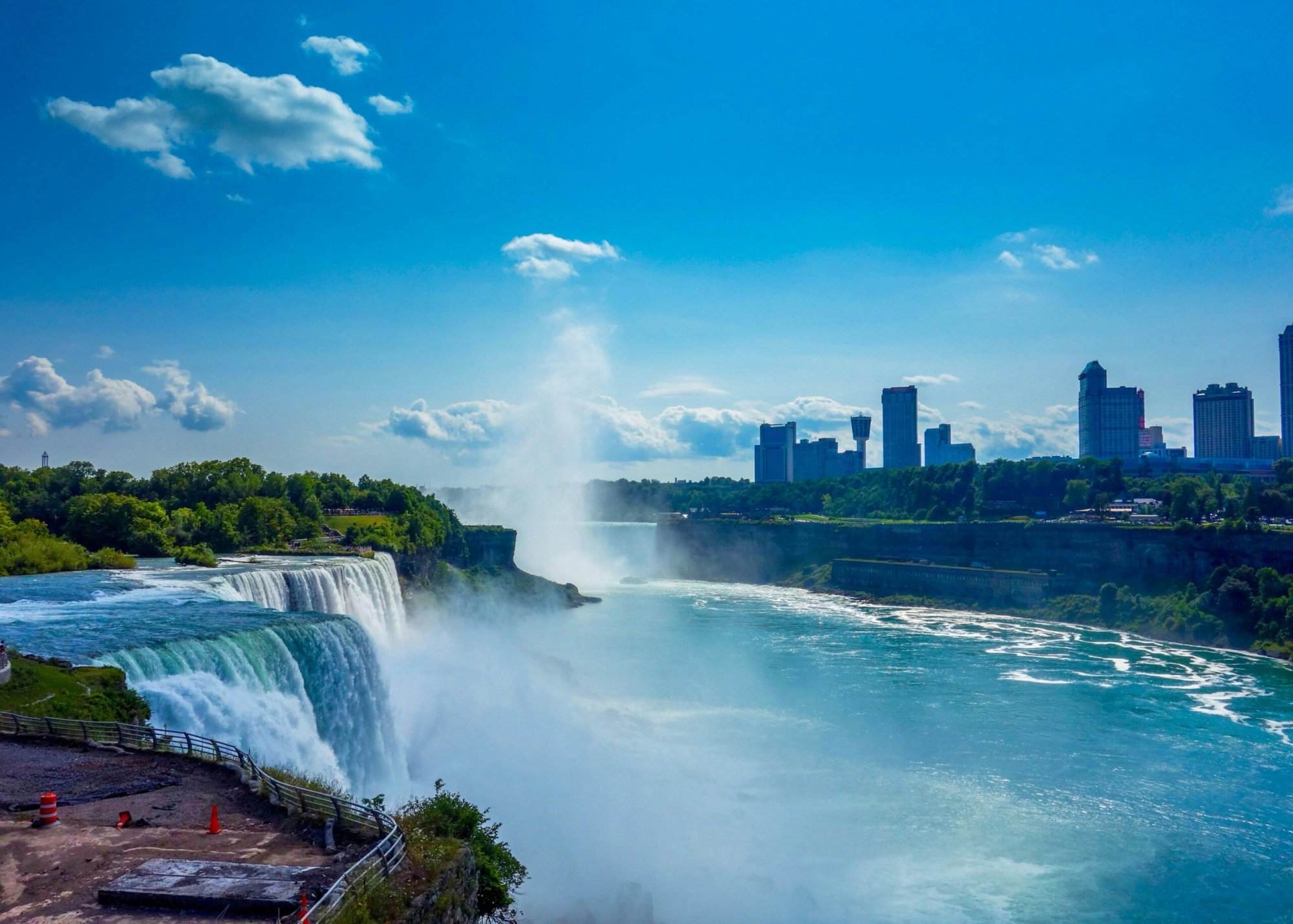 Niagara Falls on a clear day, with mist rising from the waterfall and a marathon scene in the background.