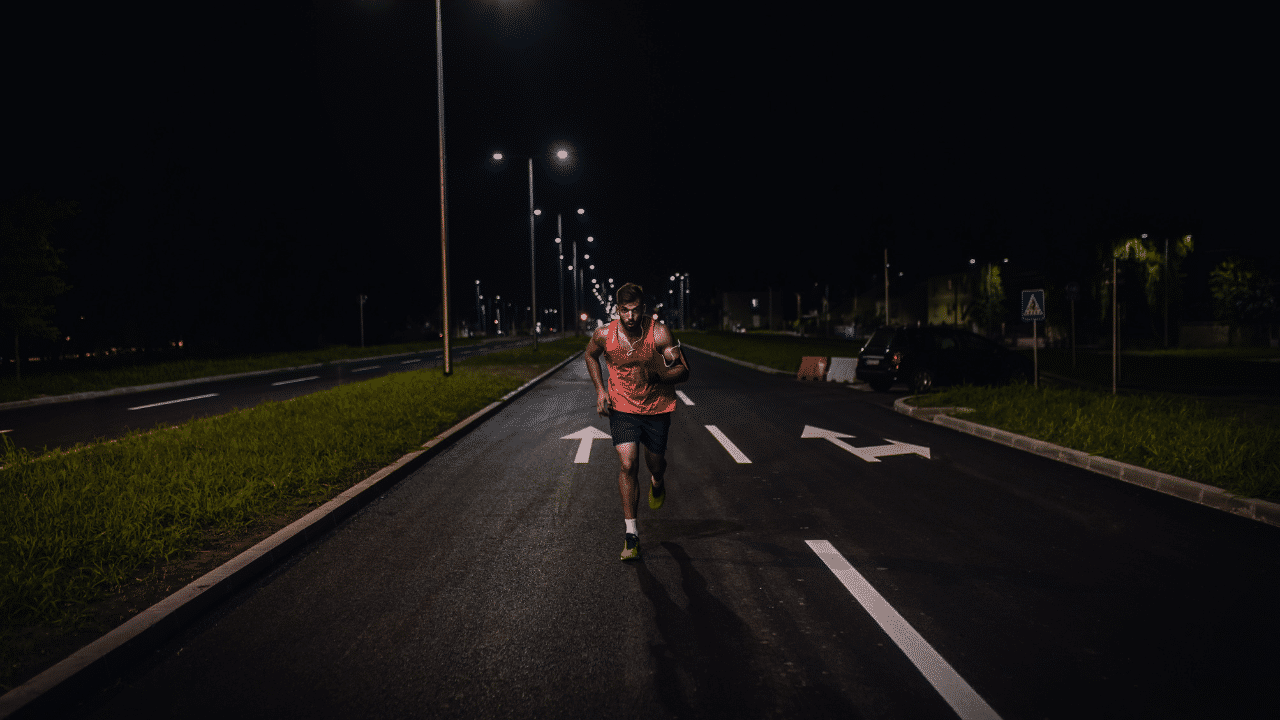 A person in athletic gear runs on a well-lit, empty street at night, reminiscent of a Wings For Life World Run. The street lights and road markings are clearly visible.